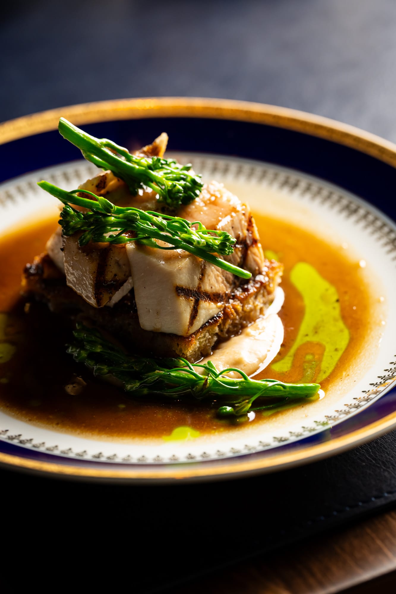 Grilled fish with broccolini and golden broth on navy china