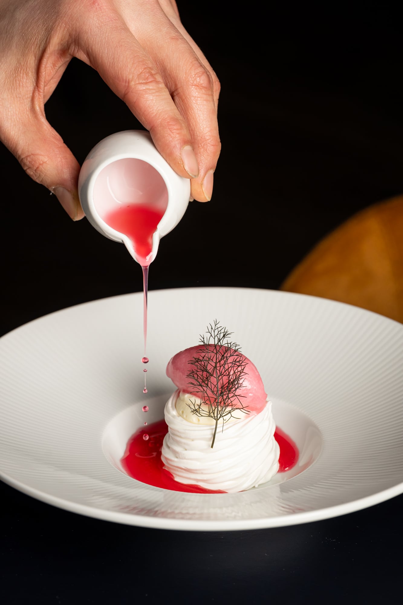 Hand pouring pink sauce over meringue dessert